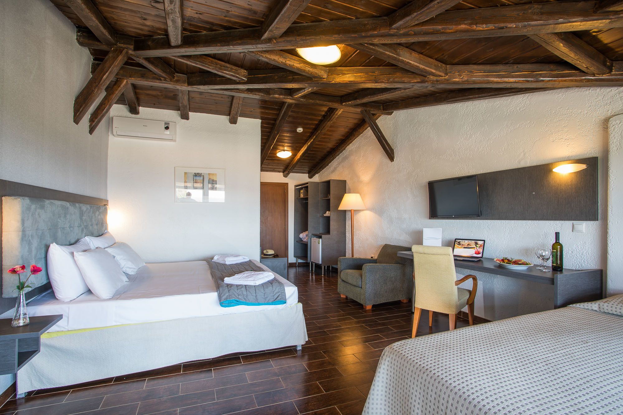 Ein gemütliches Zimmer mit einem Bett, einem Schreibtisch und einem Stuhl. Ein Fernseher ist an der Wand befestigt und auf dem Schreibtisch steht eine Lampe.