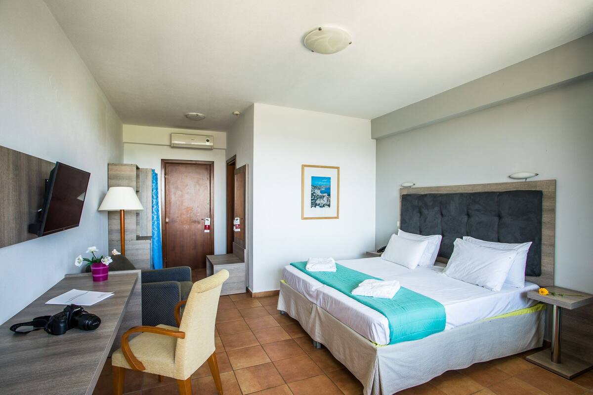 Ein Hotelzimmer mit Bett, Schreibtisch, Stuhl, Fernseher und einem Bild an der Wand.