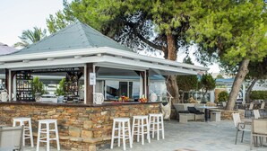 Zona de bar al aire libre con paredes de piedra, taburetes blancos y una mesa de madera.