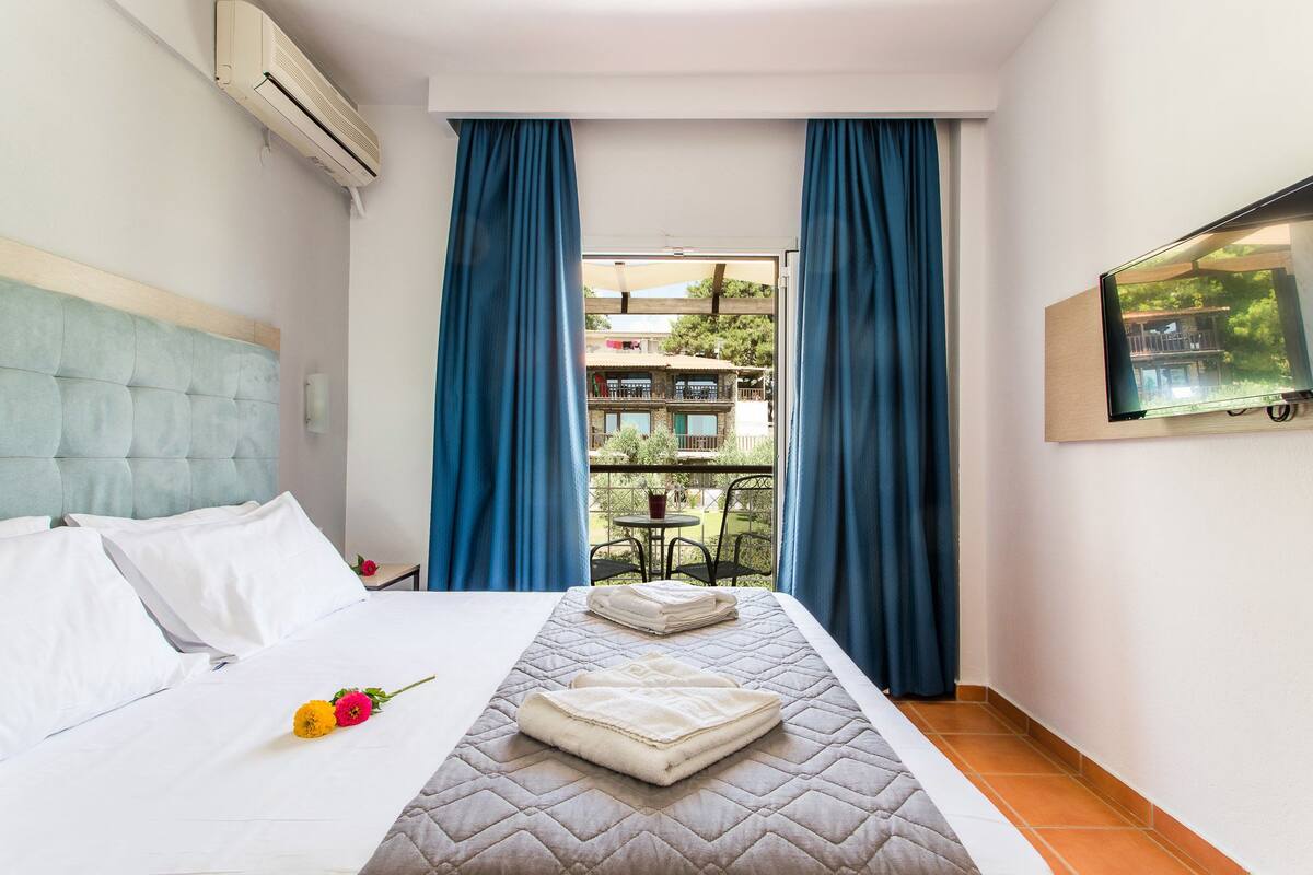 Ein Hotelzimmer mit einem Bett, Balkonblick und einem an der Wand befestigten Fernseher.