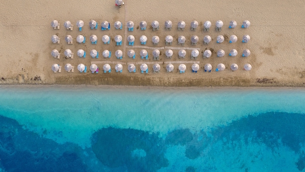 Vista aérea de una playa con hileras de sombrillas y una extensión de agua azul cristalina.