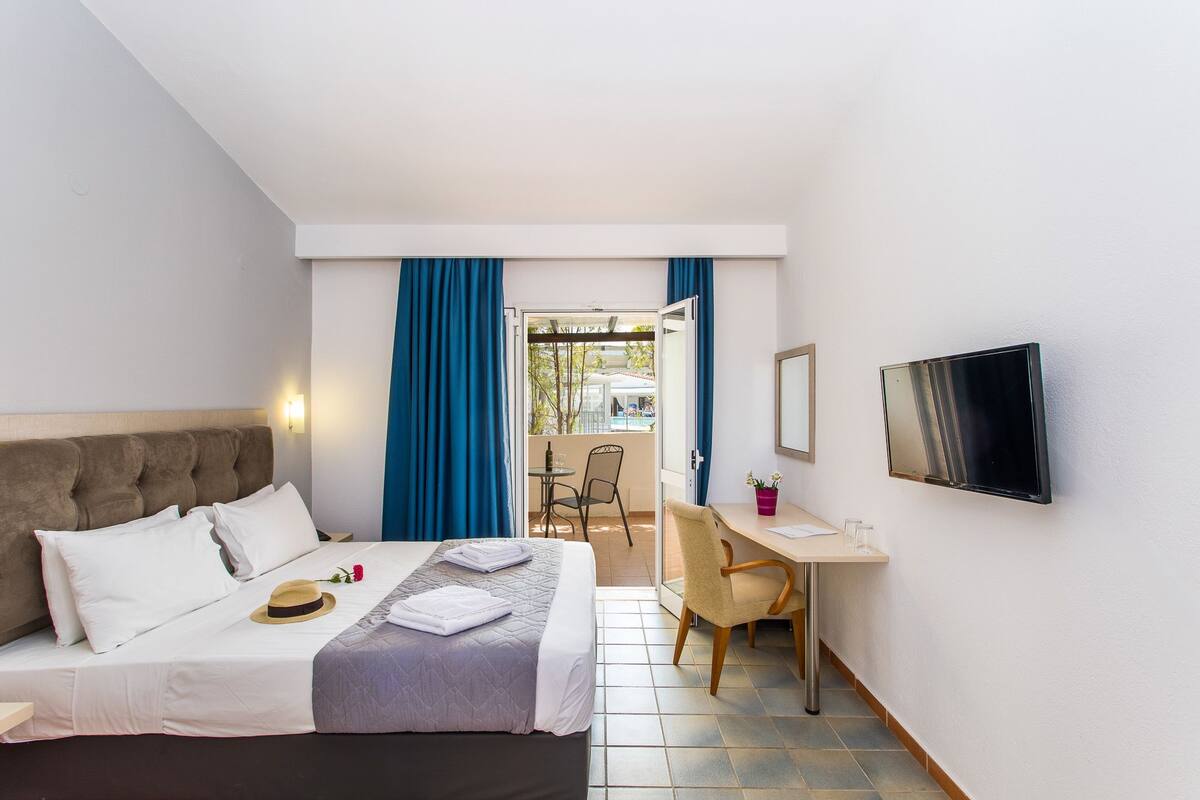 Ein Hotelzimmer mit Bett, Schreibtisch, Stuhl, Fernseher und Blick auf einen Außenbereich.