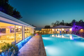 Un área de piscina moderna al aire libre con un comedor acristalado y un salón cubierto.
