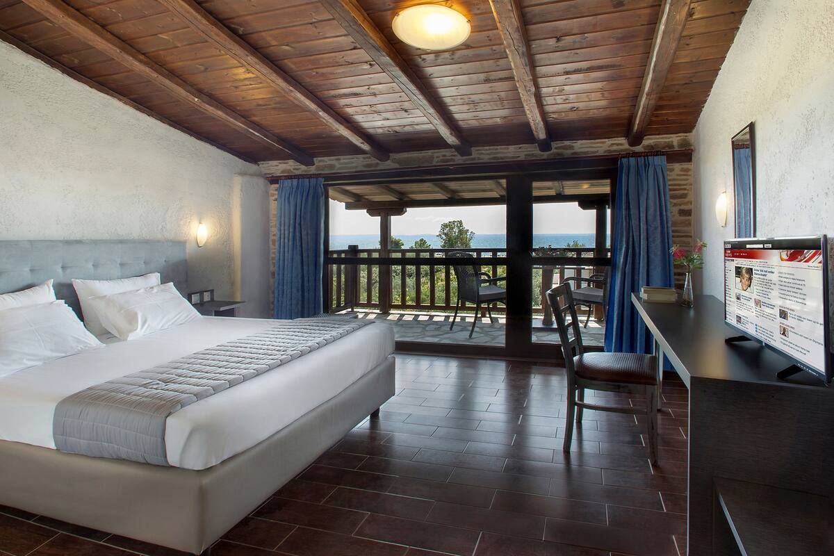 Ein Schlafzimmer mit einem großen Bett, Holzboden und einem Balkon mit Blick.