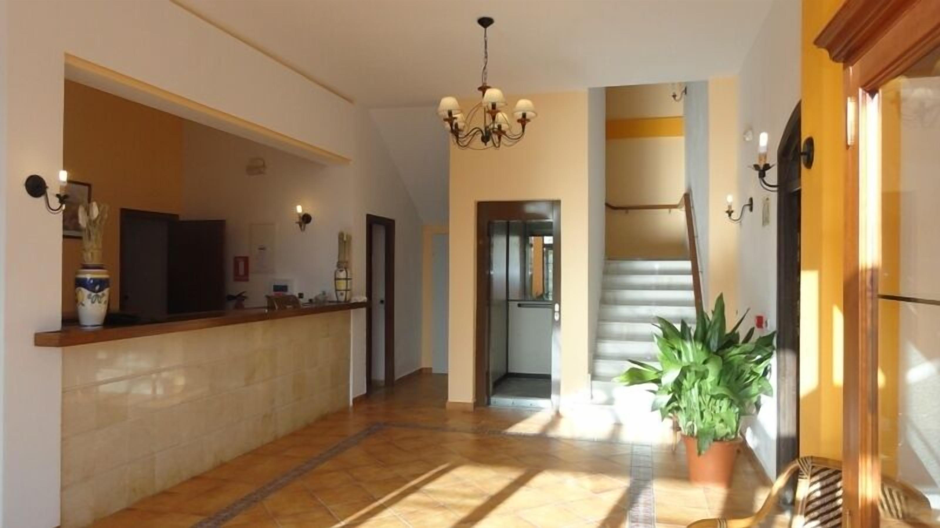 A spacious hallway with a reception desk, a chandelier, and a staircase leading to an upper floor.