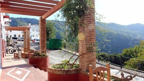 Un espacio de estar al aire libre cubierto, con pilares de ladrillo, plantas en macetas y vistas a un paisaje montañoso.
