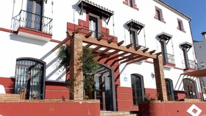 Un edificio con fachada roja y blanca, una pérgola de madera y una escalera que conduce a la entrada.