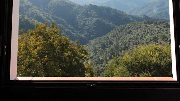 Vista a través de una ventana de un paisaje montañoso con abundante vegetación y colinas lejanas.