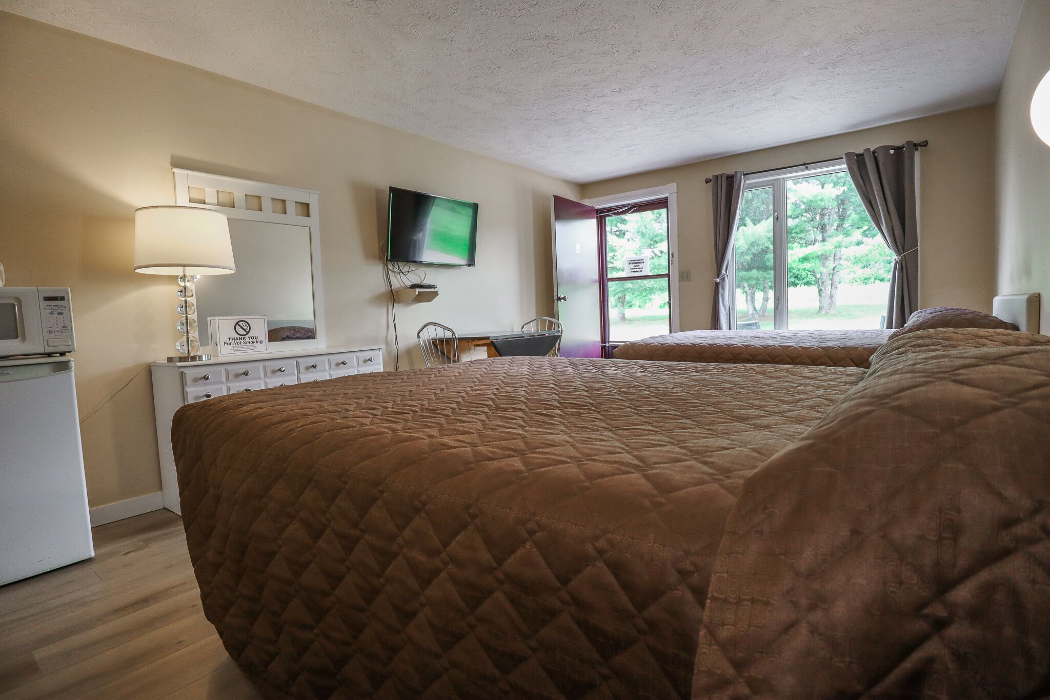 Habitación de hotel con una cama grande, un escritorio con silla, televisor montado en la pared y una ventana con cortinas.