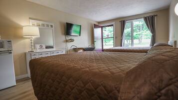 Habitación de hotel con una cama grande, un escritorio con silla, televisor montado en la pared y una ventana con cortinas.
