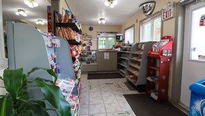 Interior de una tienda de comestibles con estantes llenos de productos, un refrigerador y una señal de salida.