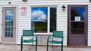 Un motel con dos sillas verdes afuera, una puerta de tormenta y un letrero de advertencia sobre hielo y nieve.