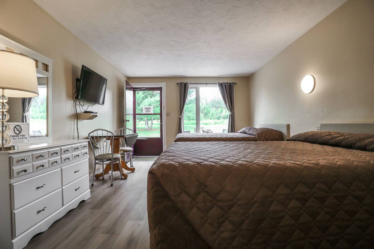 A bedroom with a large bed, a TV mounted on the wall, a dresser, and a chair.