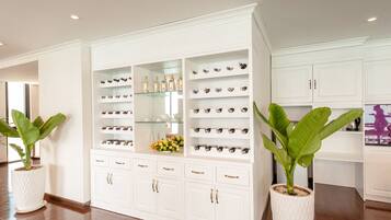 A spacious room with a large white cabinet filled with various items, including bottles and decorative pieces. There are two large potted plants, one on each side of the cabinet.