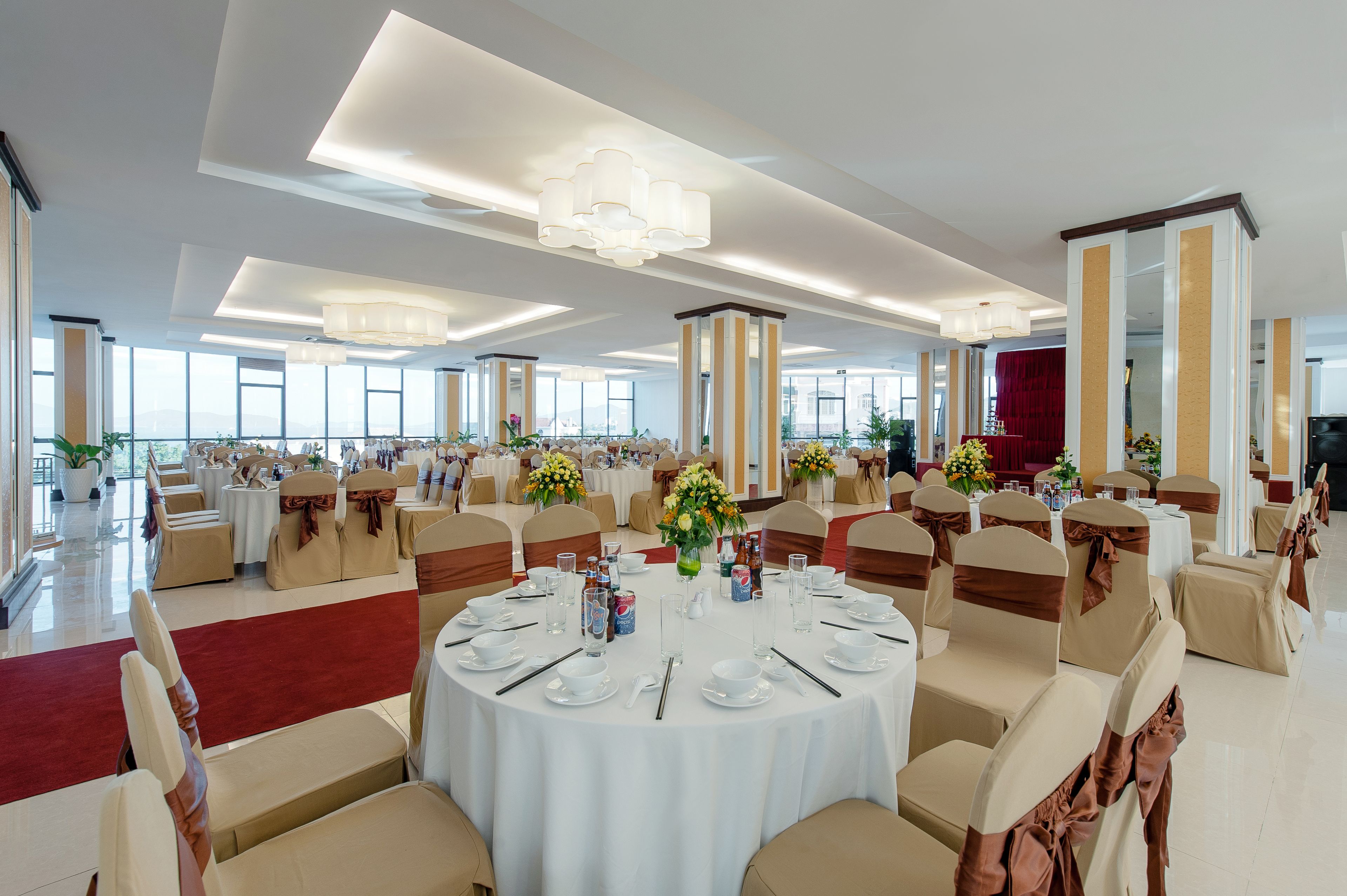 A banquet hall with round tables, chairs, and floral centerpieces.
