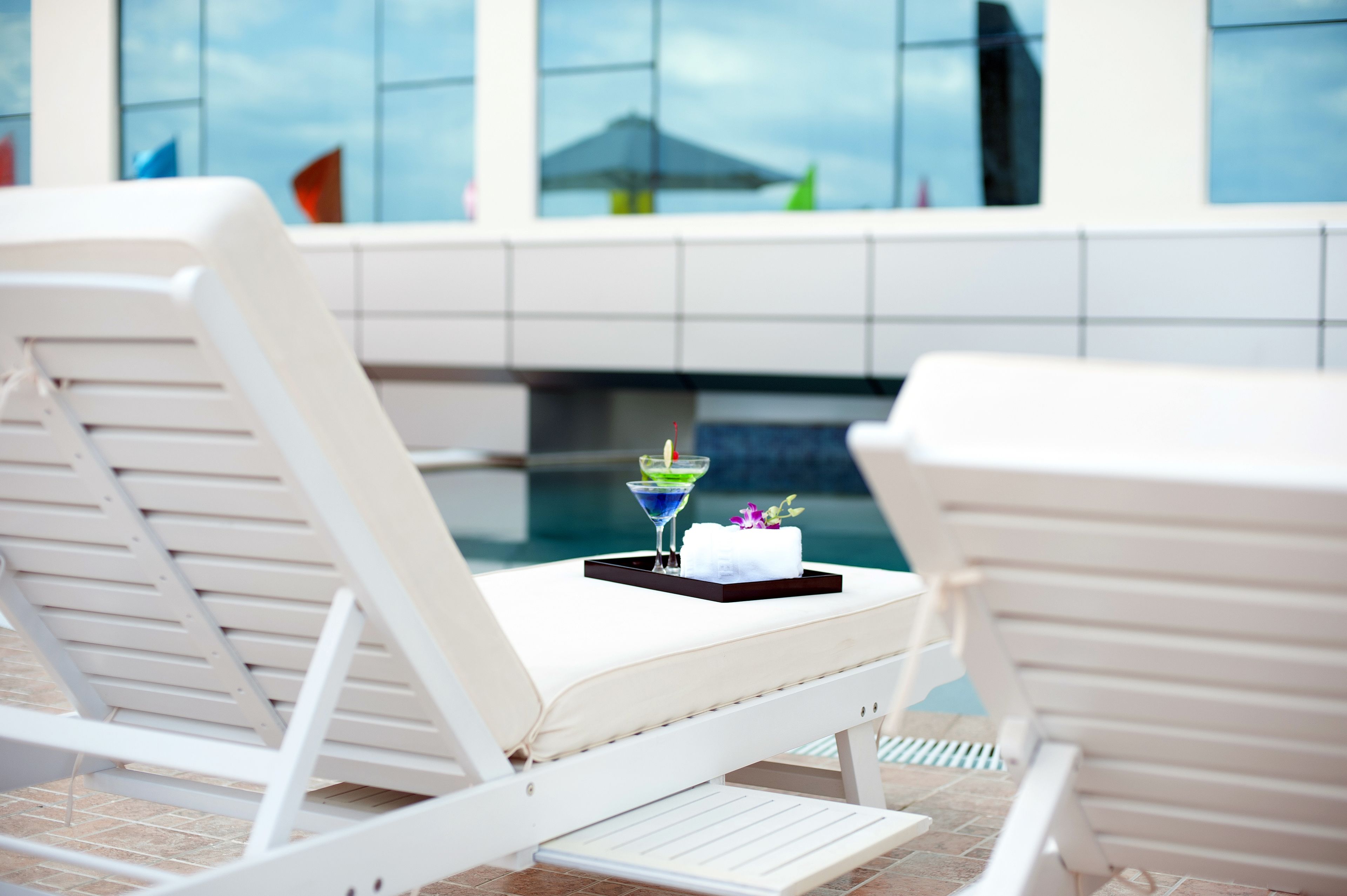 Two white lounge chairs with a tray table, a martini glass, and a towel on one of the chairs.