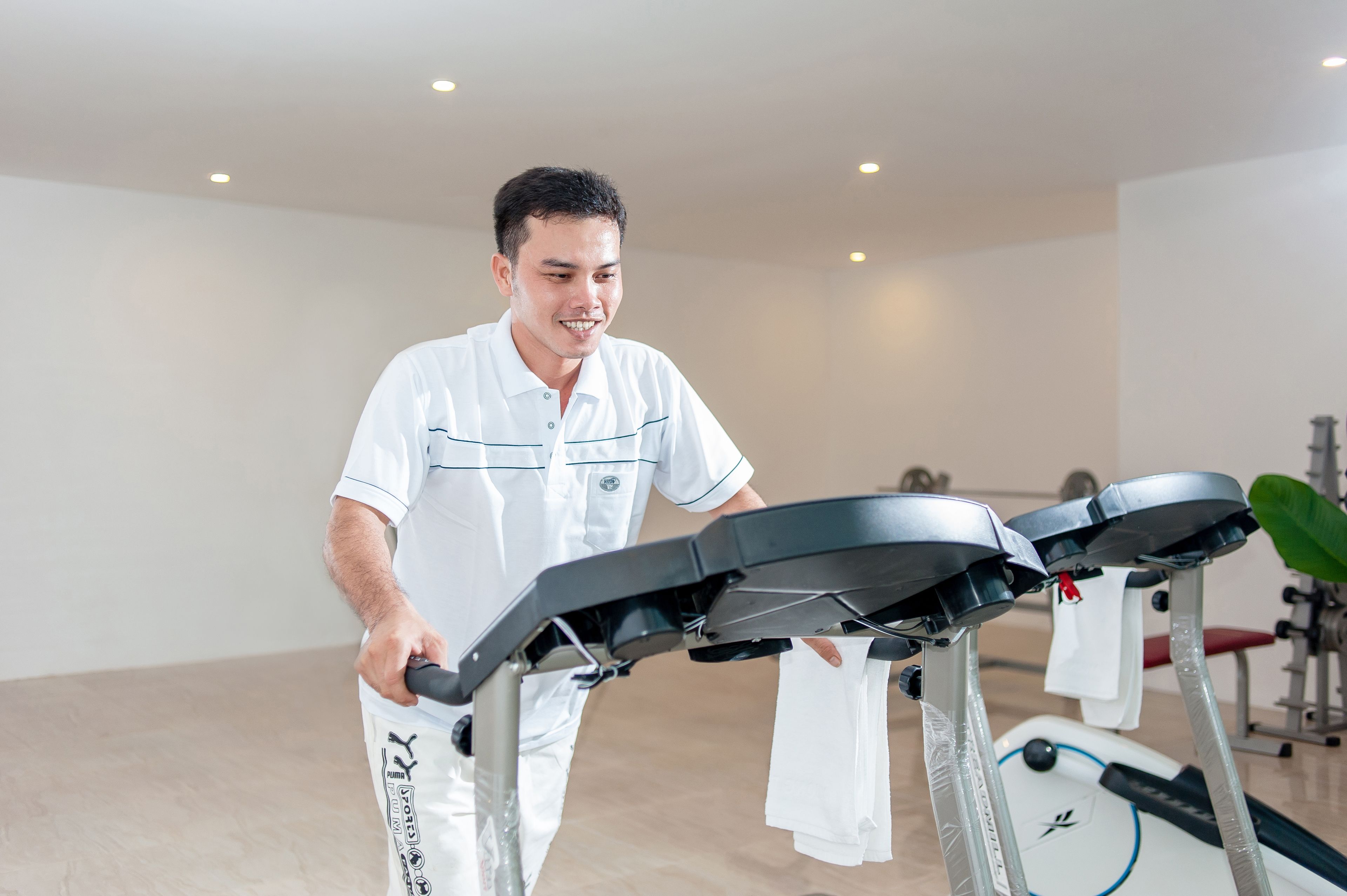 A person using a stationary bike in a gym with a treadmill and weights in the background.