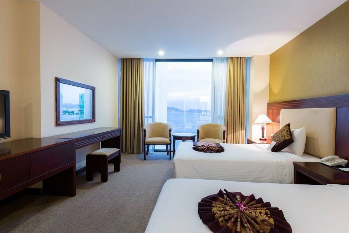 A hotel room with two beds, a desk, a TV, and a view of the city.