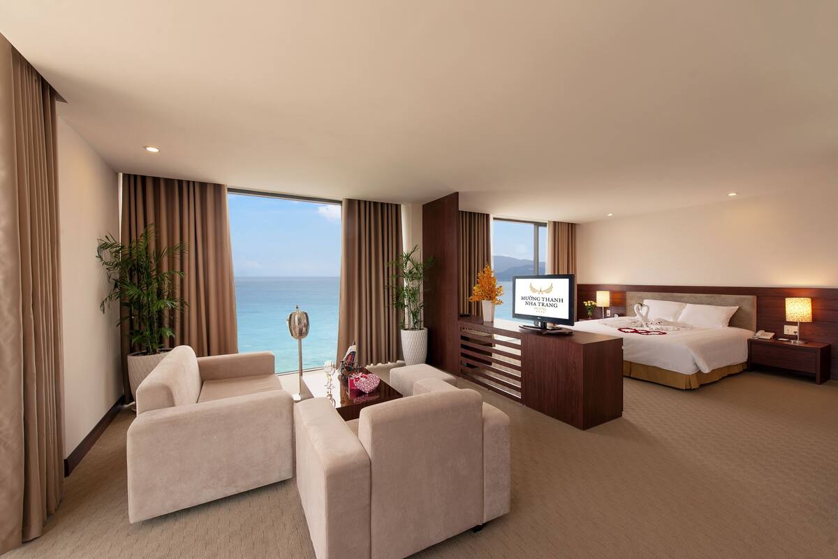 A hotel room with a bed, a TV, a desk, a sofa, and a view of the ocean.