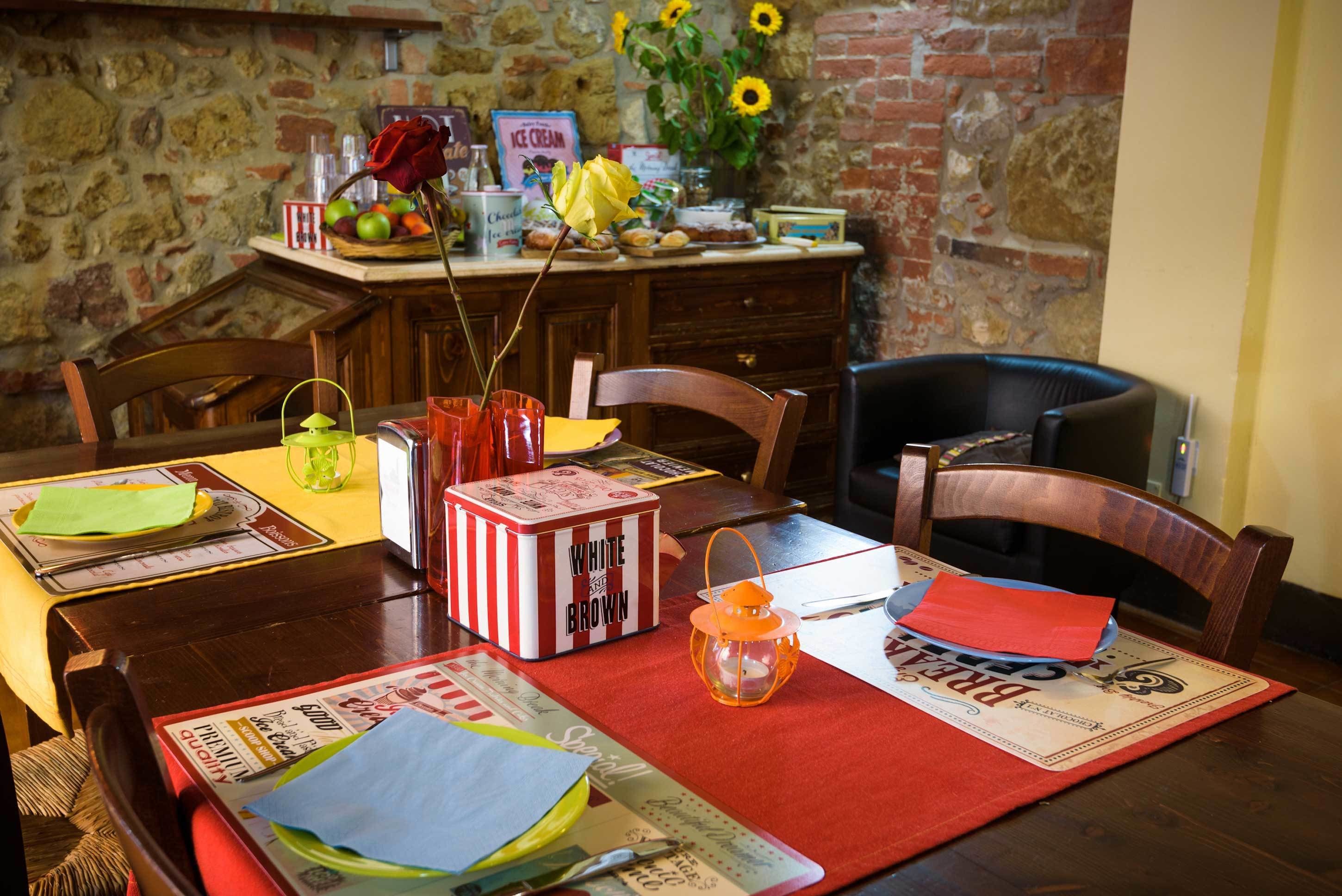 Zona pranzo con tavolo di legno apparecchiata per due, con una scatola a righe, un tovagliolo rosso e una lanterna.