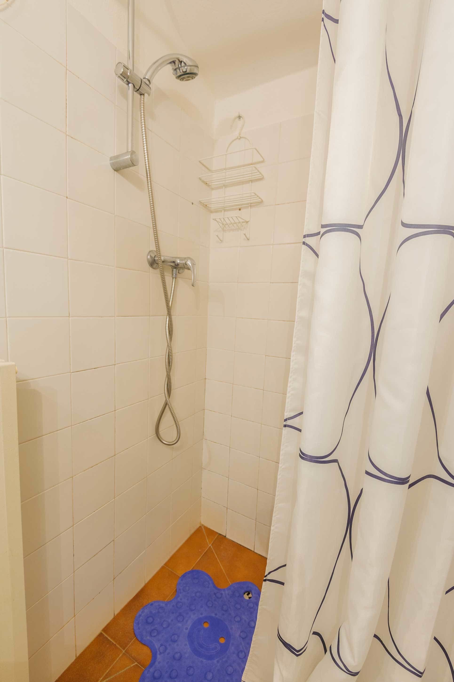 Une douche équipée d’un pommeau de douche à main, d’un porte-savon et d’un tapis de bain bleu.
