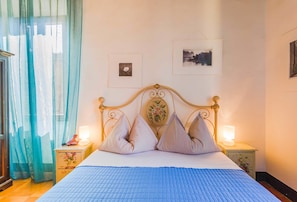 Une chambre à coucher avec un lit, des rideaux, des tables de chevet et des œuvres d’art murales.