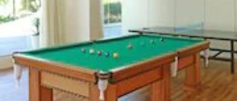 A pool table in a room with wooden flooring and large windows.