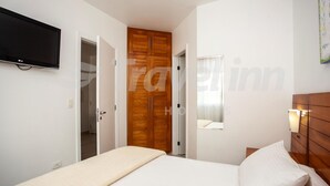 Une chambre à coucher avec un lit, une armoire en bois, une télévision et une fenêtre avec des rideaux.