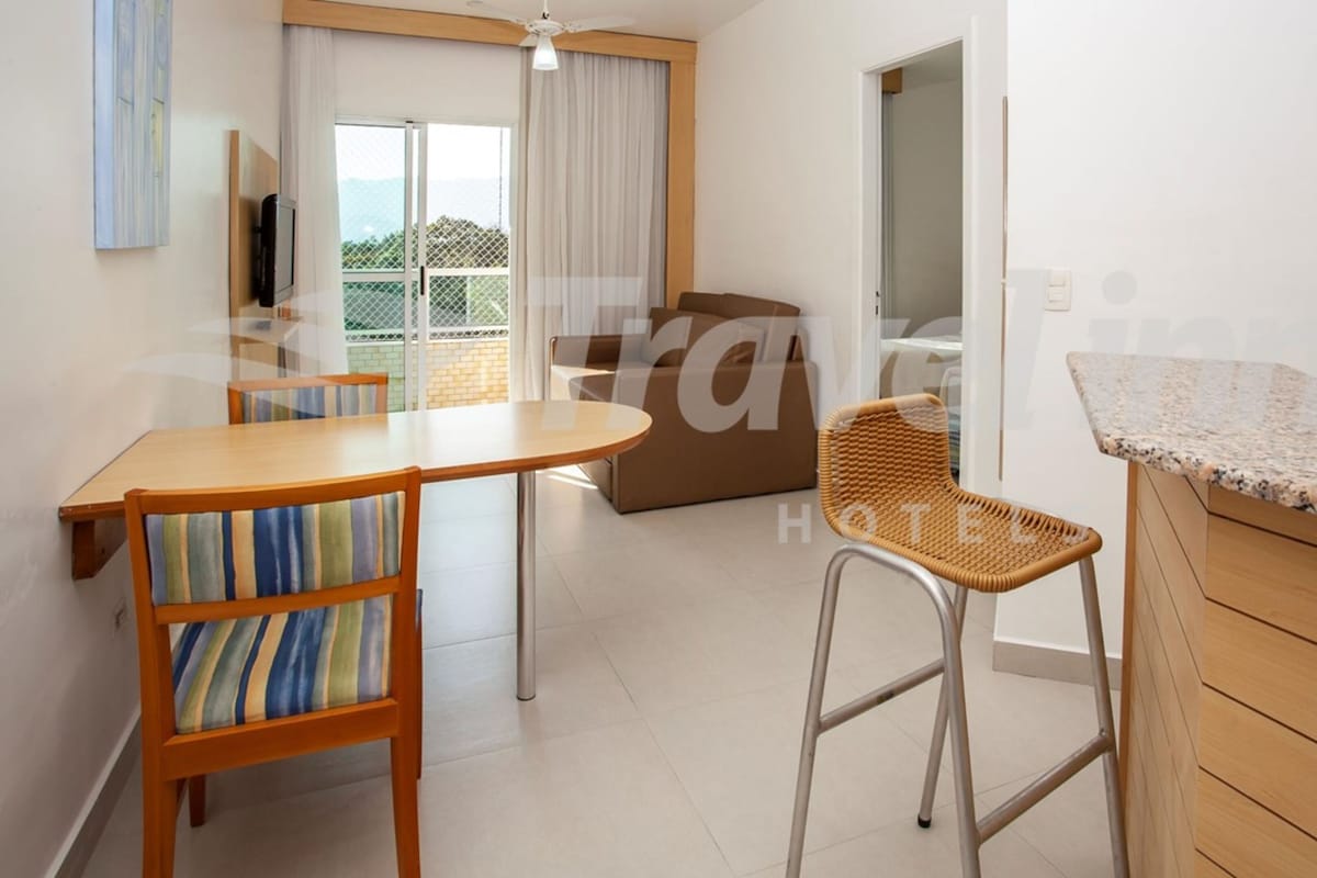 A modern hotel room with a dining area, a sofa, and a wicker chair.