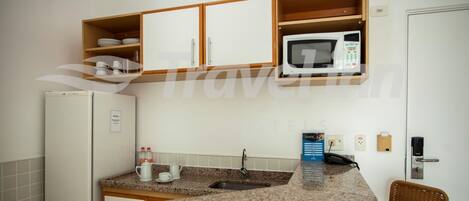 A kitchen with a microwave, a refrigerator, a sink, and a wicker chair.