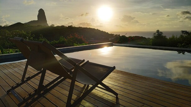 A wooden deck with a lounge chair overlooking a pool. - Colina Pousada SPA (Fernando de Noronha)