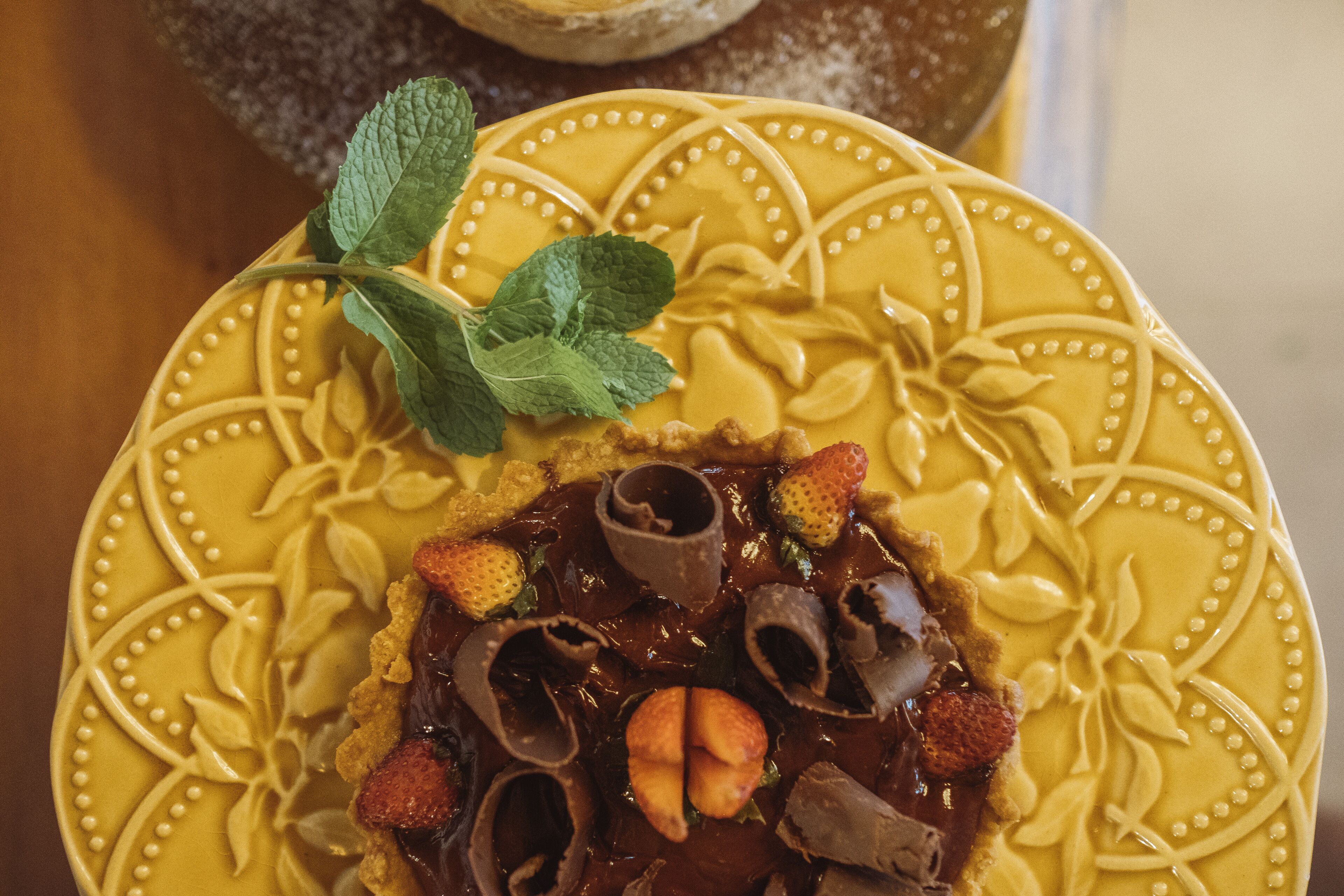 A dessert on a yellow plate with intricate designs, garnished with mint leaves and strawberries.