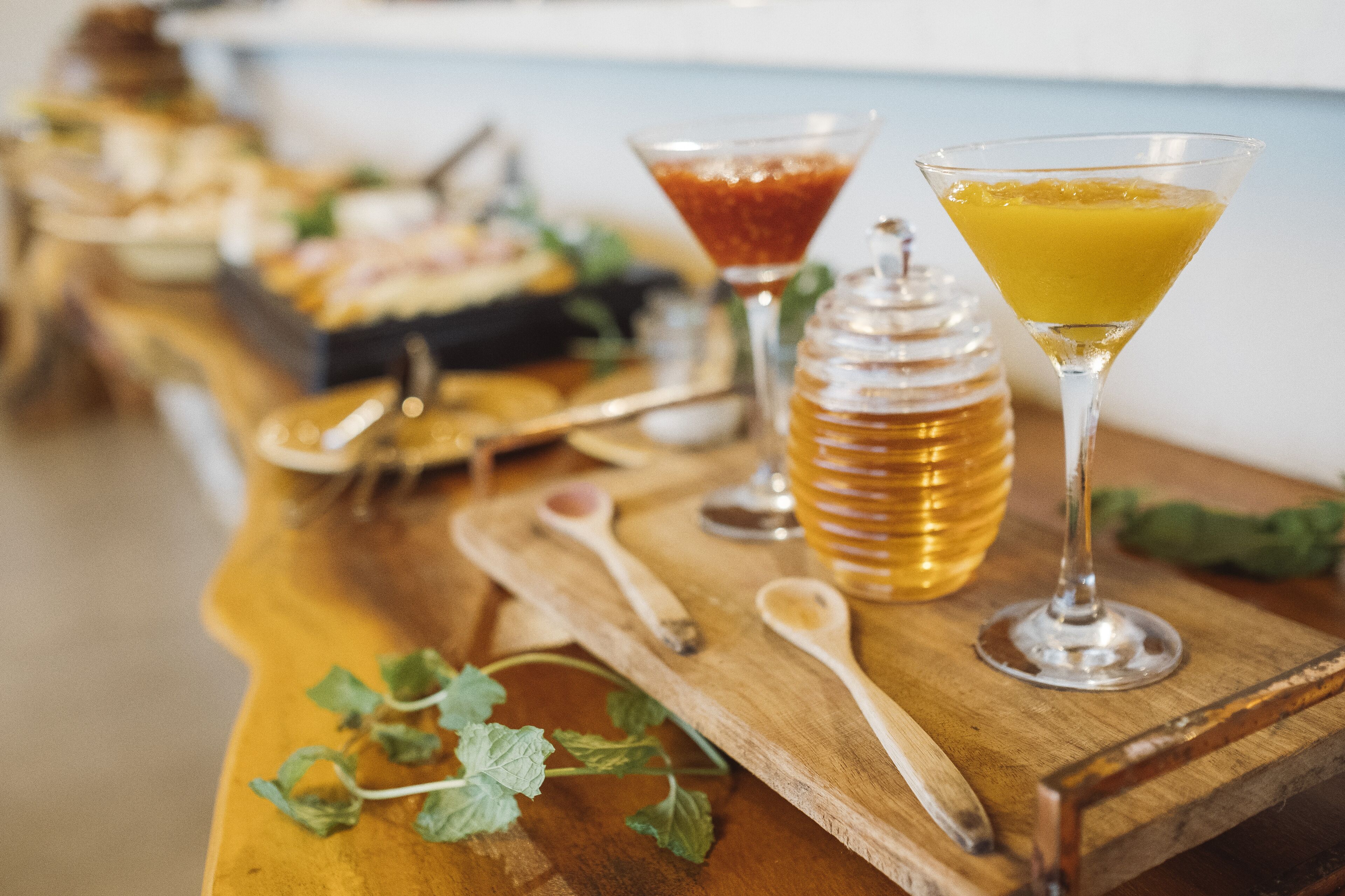 A wooden table with a variety of food items and drinks, including a martini glass with a yellow drink and a honey jar.