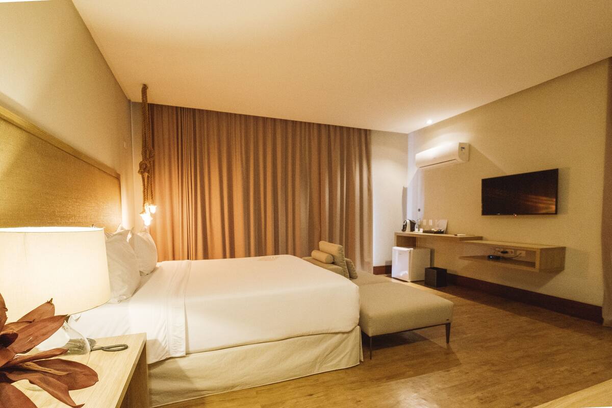 Une chambre d’hôtel comprenant un lit, une table de chevet, une lampe, des rideaux, un bureau avec une chaise et un téléviseur fixé au mur.