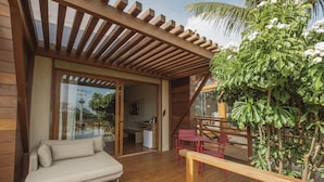 A wooden deck with a sofa and a dining table, a glass door leading to a kitchen, and a potted plant. - Colina Pousada SPA (Fernando de Noronha)