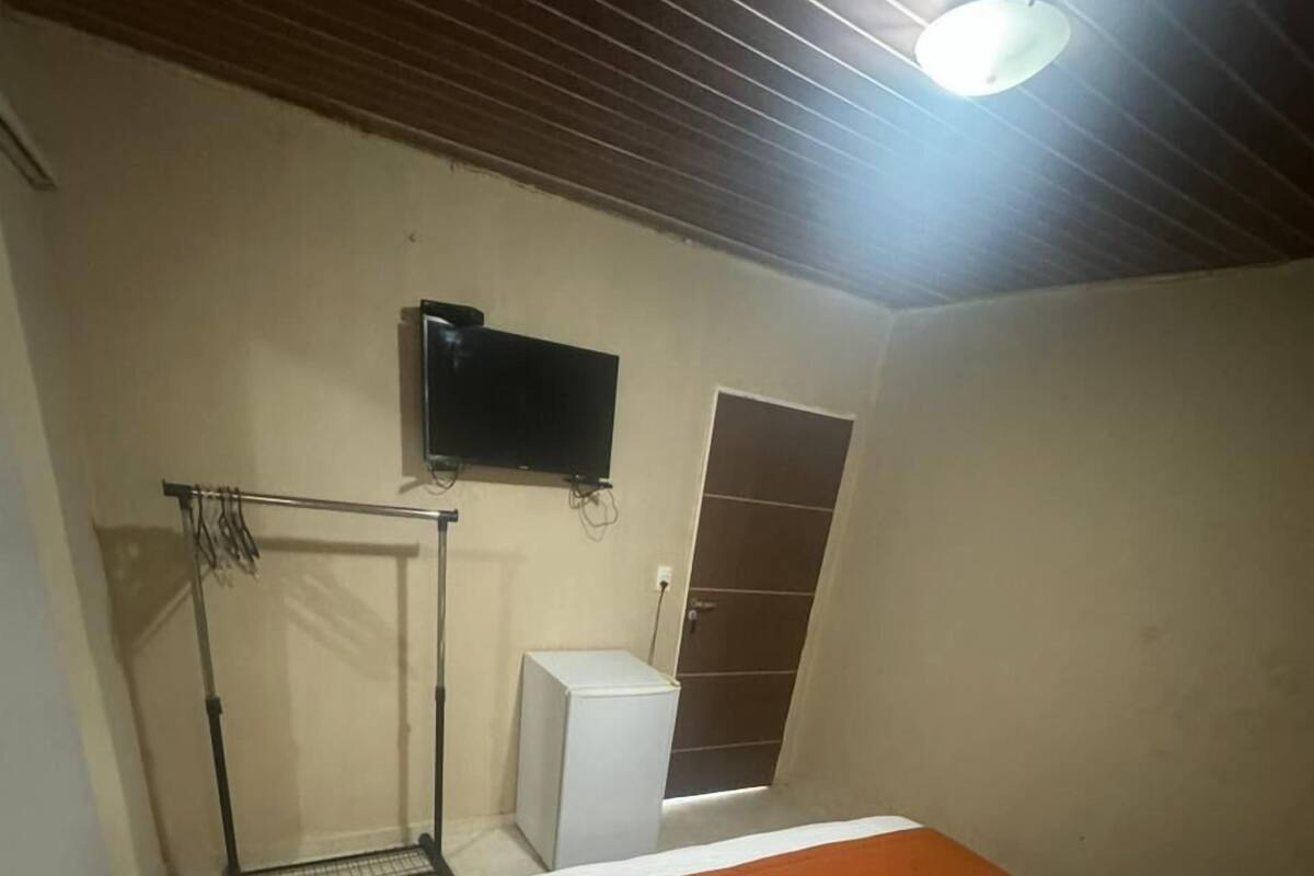A bedroom with a bed, a TV mounted on the wall, a radiator, and a door.