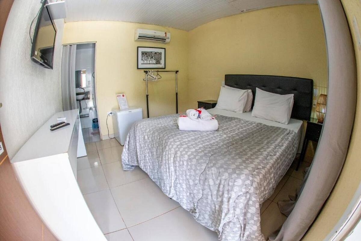 A hotel room with a bed, a desk, a chair, an air conditioning unit, and a picture on the wall.