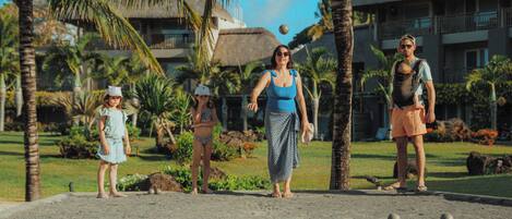 A group of people playing croquet on a sandy court with palm trees and a building in the background.