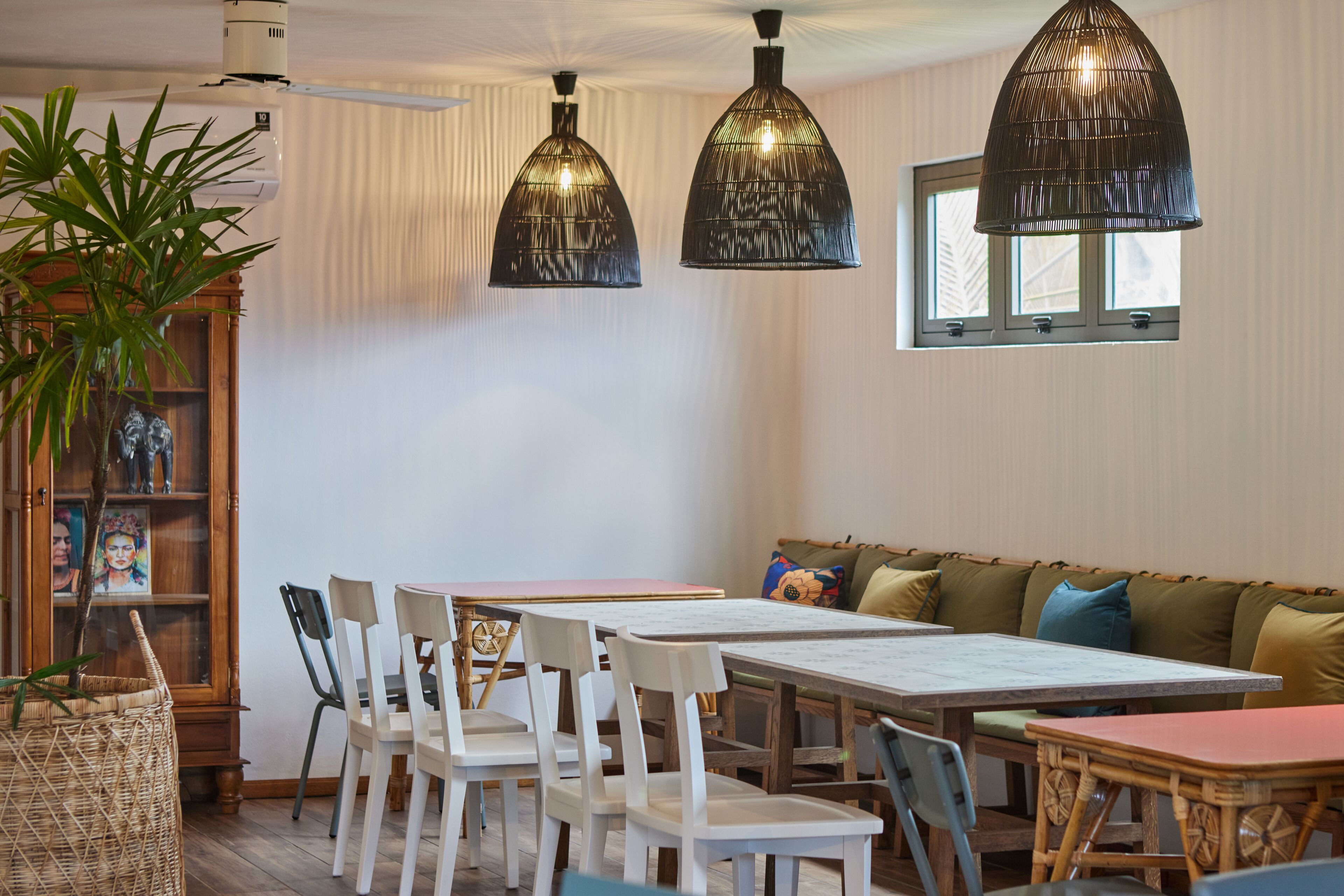 Un coin repas avec une table en bois, des chaises blanches et un banc rembourré. Deux lampes suspendues sont fixées au plafond.