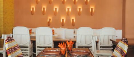 A dining area with a wooden table, white chairs, and a wall with multiple wall-mounted lights.