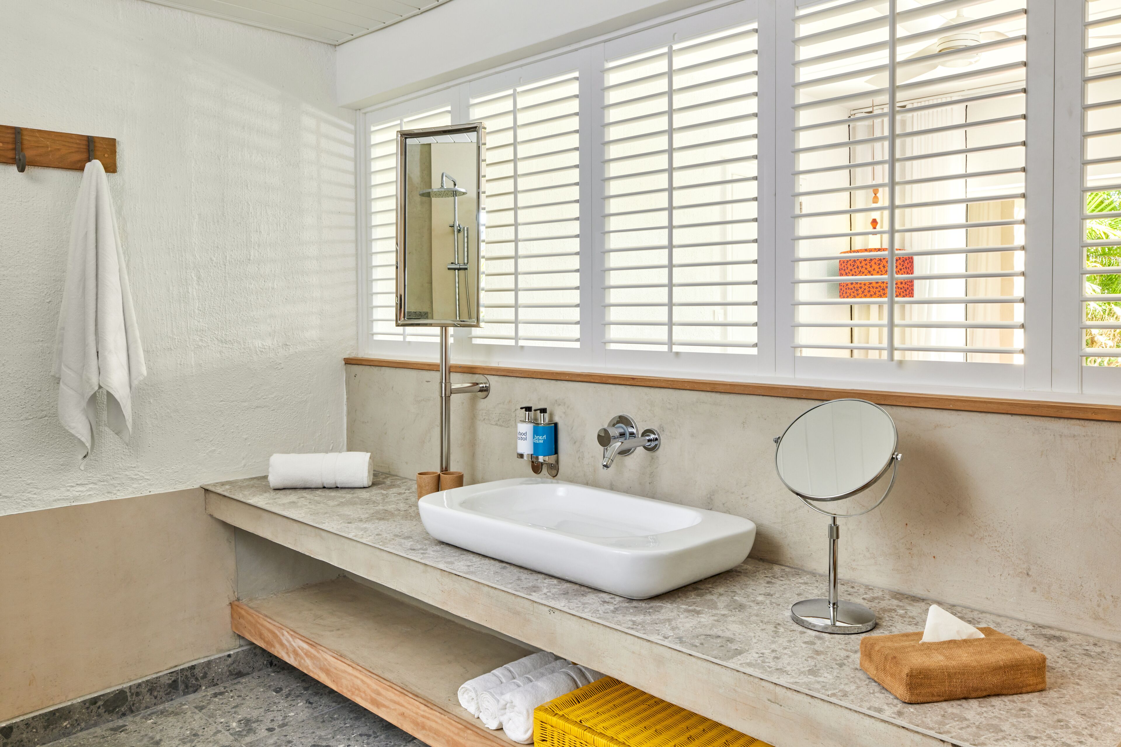 Une salle de bain avec un lavabo blanc, un miroir et une fenêtre avec des stores.