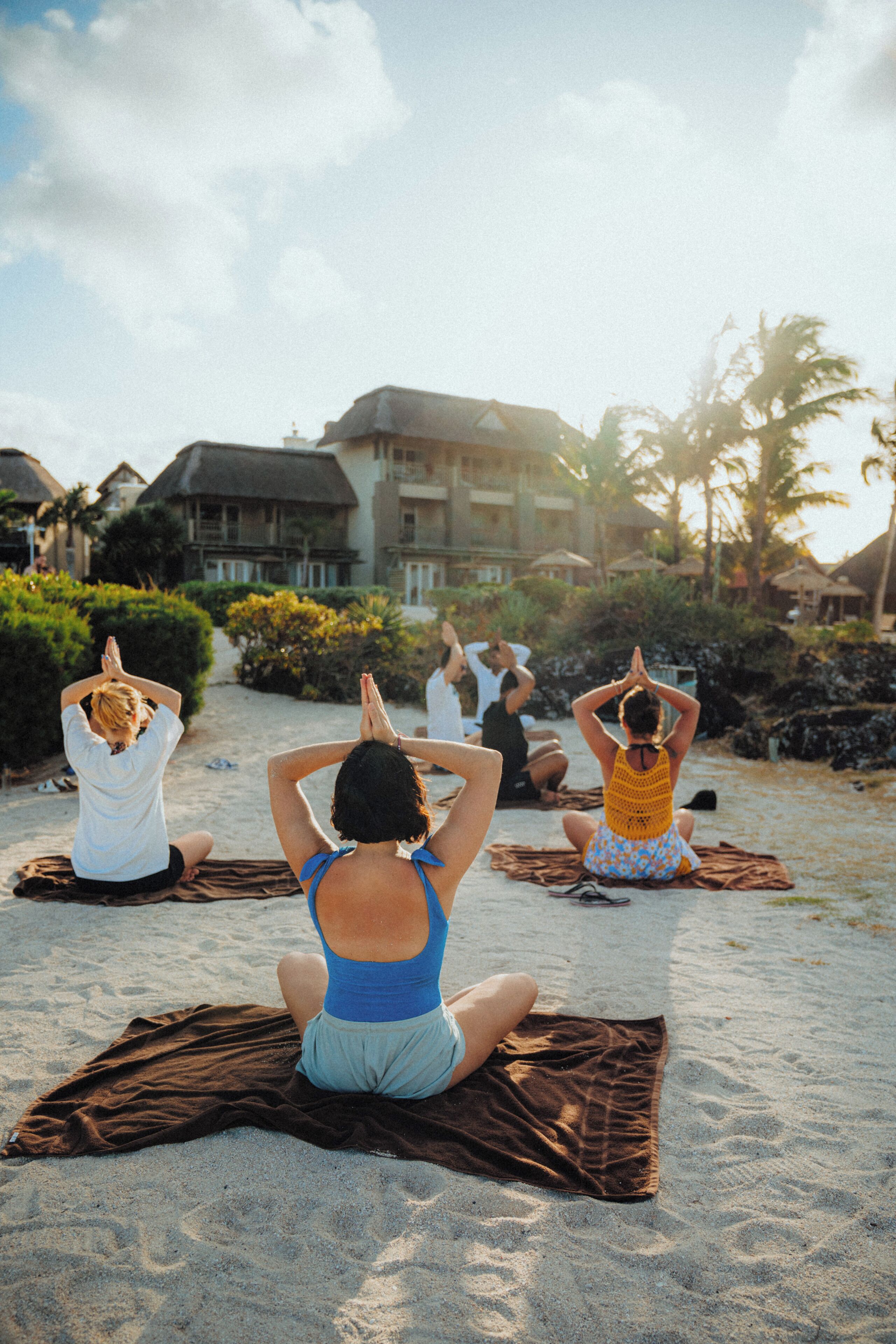 En grupp människor som utövar yoga på en strand med en byggnad i bakgrunden.