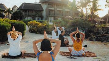 En grupp människor som utövar yoga på en strand med en byggnad i bakgrunden.