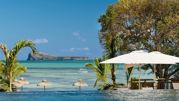 A poolside area with a view of the ocean, a boat, and a distant island. - Zilwa Attitude (Calodyne)