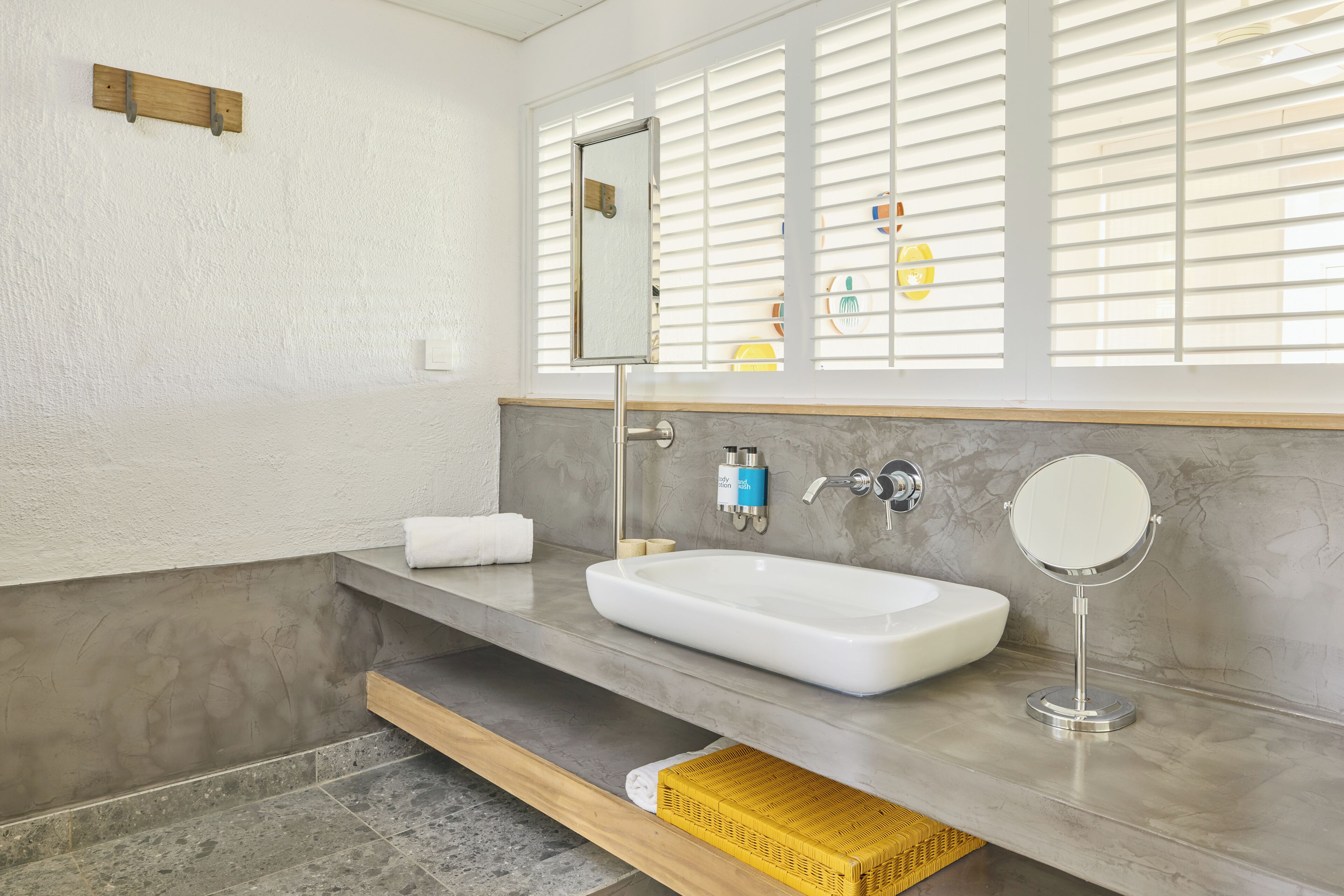A bathroom with a white sink, a mirror, and a window with blinds.