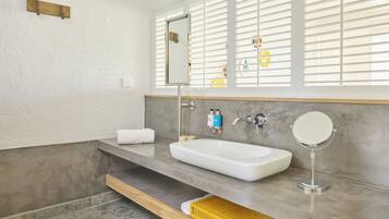A bathroom with a white sink, a mirror, and a window with blinds.