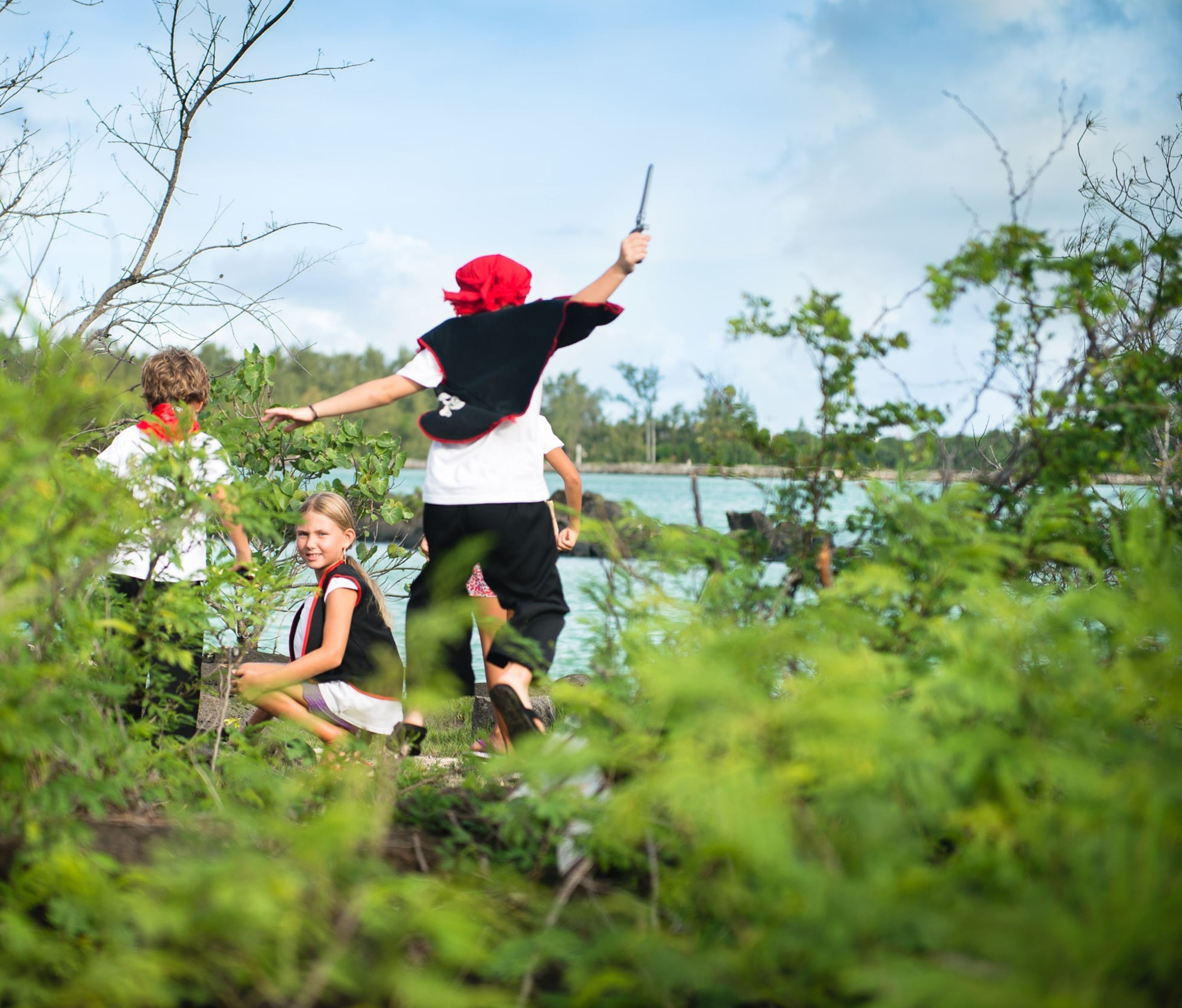 A group of people in an outdoor setting with natural vegetation and a body of water in the background.