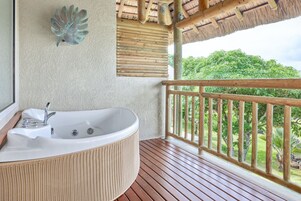 Baño con una bañera grande, terraza de madera y vistas a la vegetación.