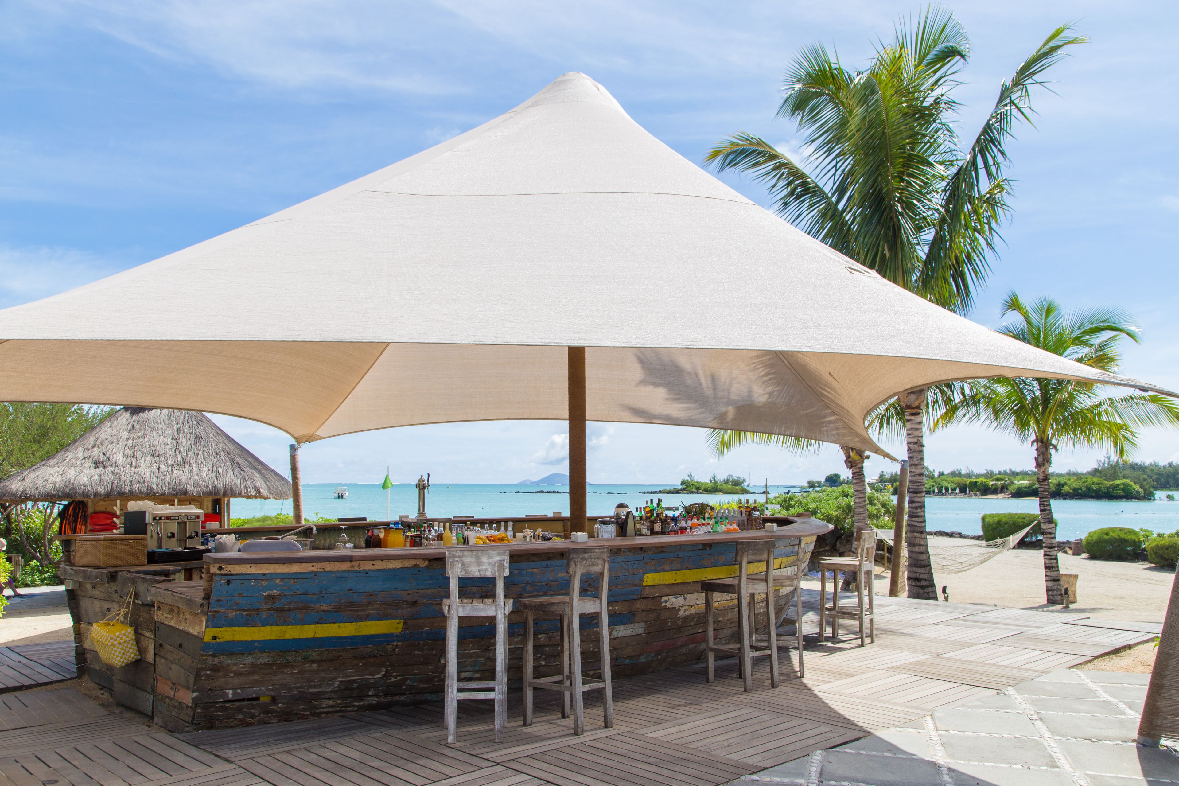 A beachside bar with a thatched roof, wooden bar counter, and outdoor seating.