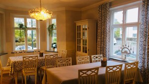 A dining area with a chandelier, white chairs, a table with a tablecloth, a cabinet, and a window with a view of the outside. - MillasVilla (Lund)